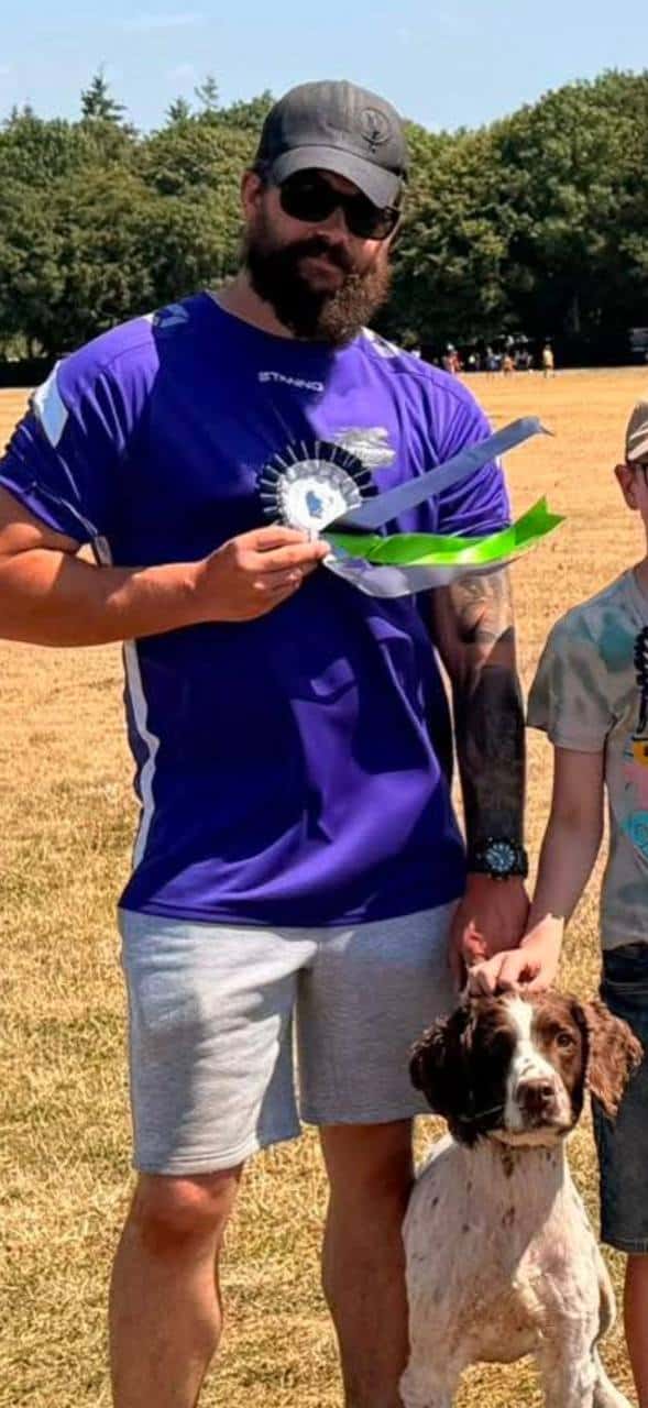 Sam in purple club kit holding a rosette, with Percy